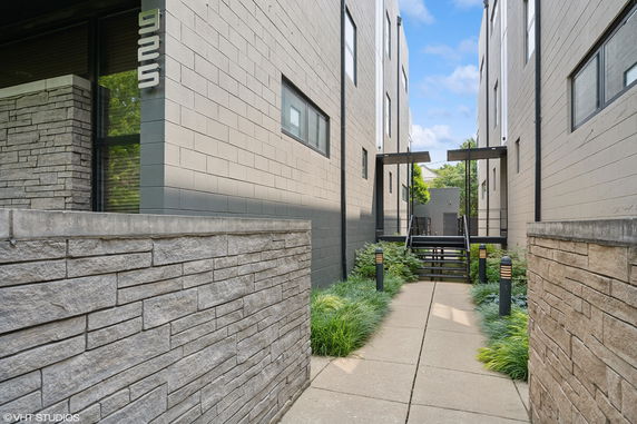 View of a modern building with light gray brick walls and a walkway between two sections.