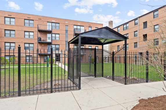 Front view of a multi-story brick apartment building with fenced entrance.