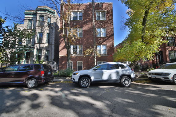 Front view of a multi-story brick building with parked cars in front.