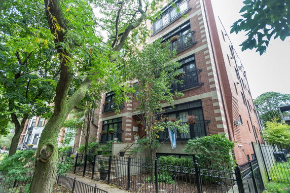 Front view of a multi-story brick building with balconies, surrounded by trees.