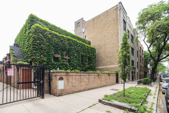Front view of a building covered in green ivy with a brick exterior and gated entrance.