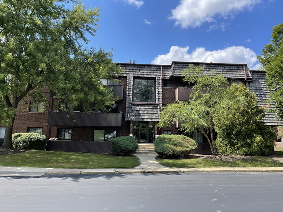 Front view of a multi-story residential building with balconies and shingled roof.