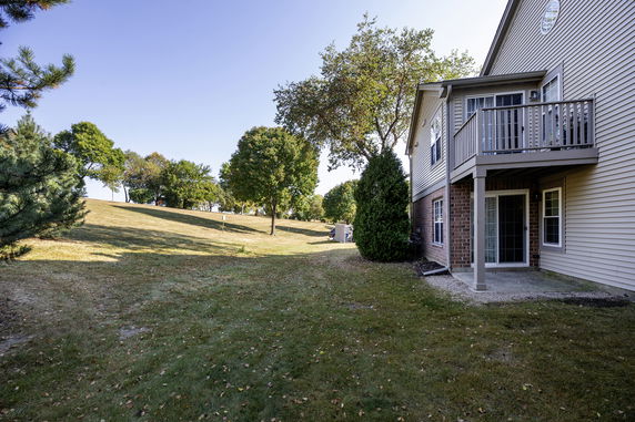 Side view of a house with a balcony overlooking a grassy area with trees.