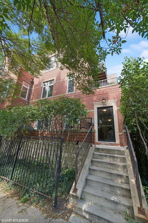 Front view of a brick multi-story building with stairs leading to the entrance.