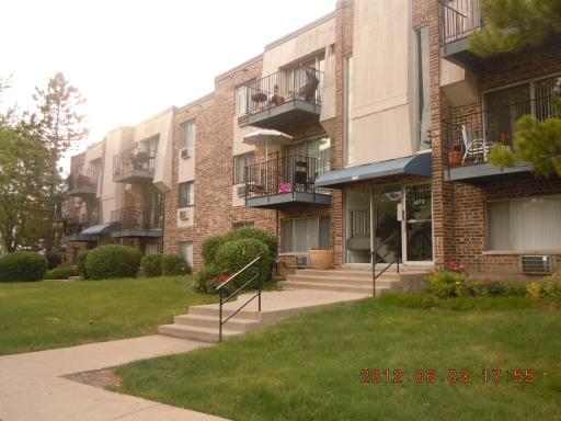 Front view of a multi-story apartment building with balconies and steps leading to the entrance.