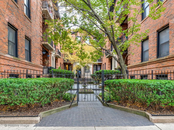 Front view of a brick apartment building with a gate and pathway.