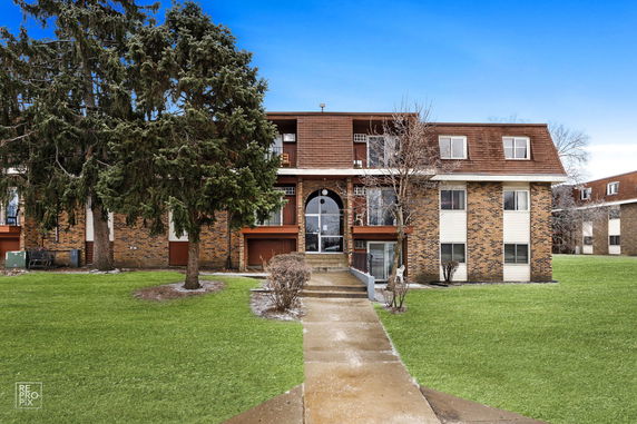 Front view of a multi-story apartment building with a brick facade and an entrance walkway.