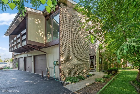 Front view of a modern multi-story house with brick and panel siding, featuring a balcony and three garage doors.