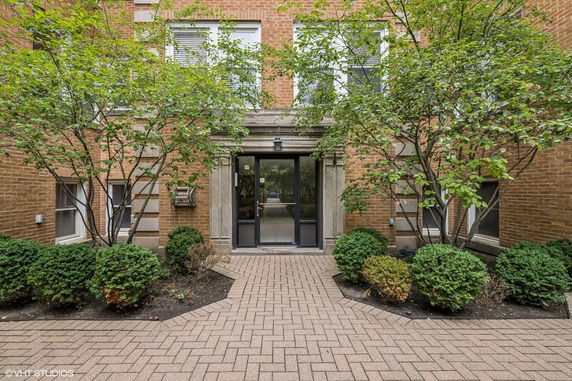Front view of a building entrance with a pathway lined by shrubs.