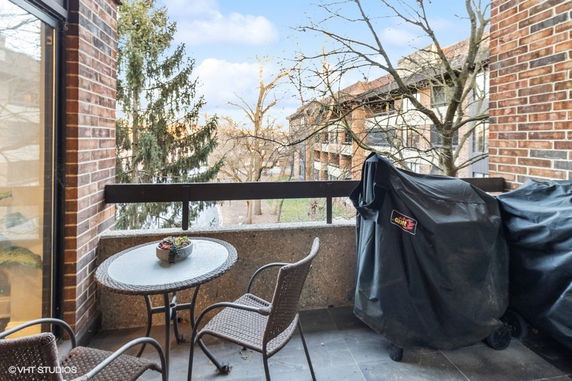 Balcony with patio furniture overlooking nearby buildings and trees.