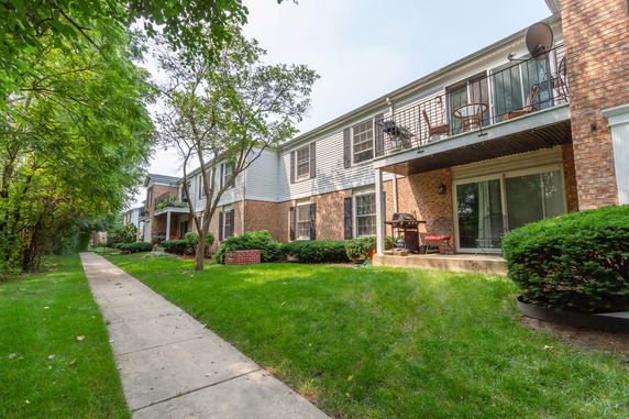 Front view of a two-story brick apartment building with balconies and a well-maintained garden area.