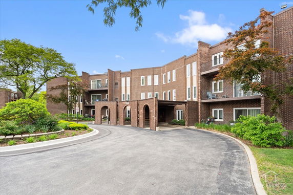 Front view of a three-story brick apartment building with balconies and a driveway.