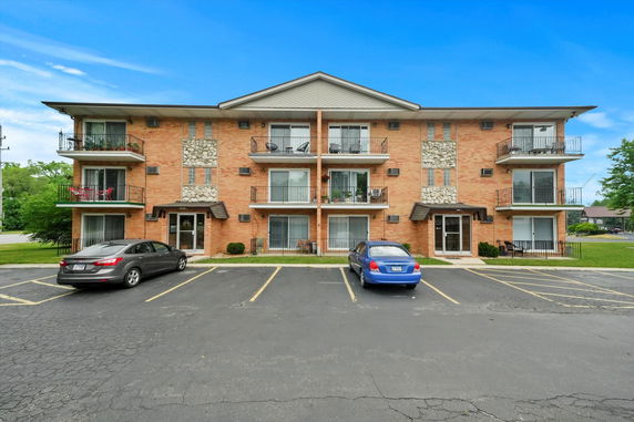 Front view of a multi-story apartment building with balconies and parking spaces.