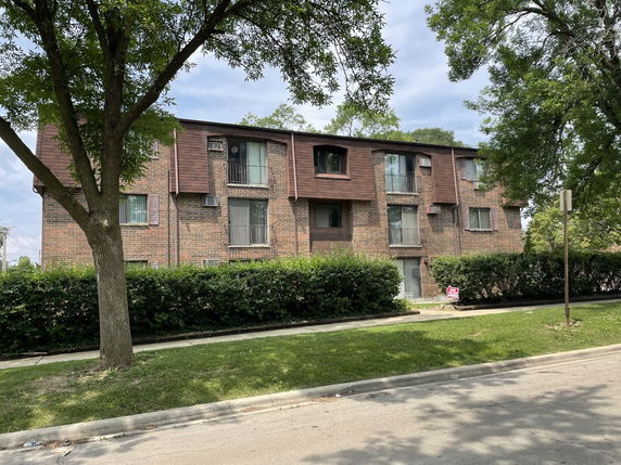 Front view of a three-story apartment building with brick exterior and windows with brown shutters.