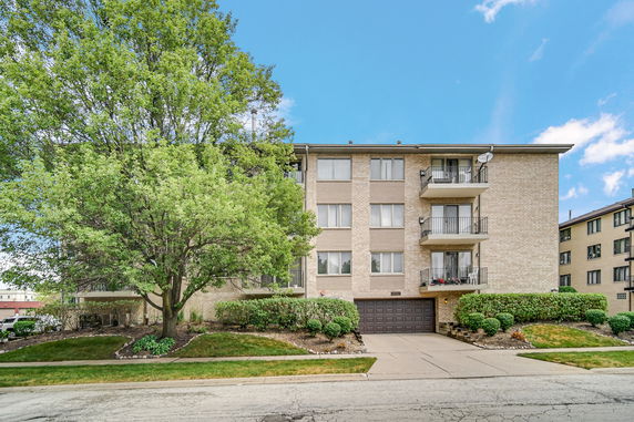 Front view of a multi-story apartment building with balconies and a garage entrance.
