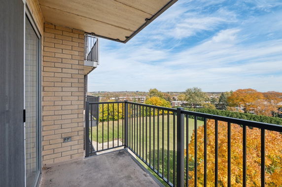 View from a balcony showing a landscaped area with trees and buildings in the distance.