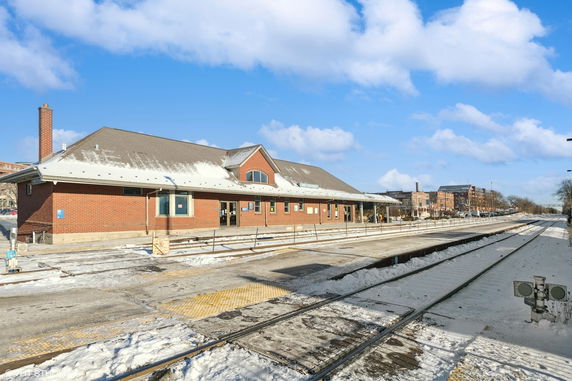 View of a brick building at a train station with snowy tracks in the foreground.