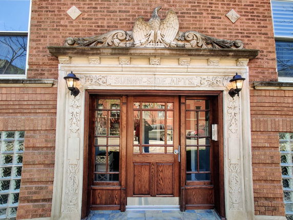 Front view of a brick apartment building entrance with decorative stonework and wooden doors.