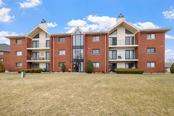 Front view of a multi-story brick apartment building with balconies.