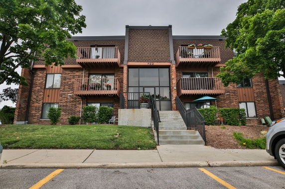 Front view of a multi-story brick apartment building with balconies and stairs leading to the entrance.