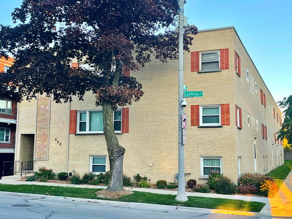 Front view of a multi-story apartment building with beige brick exterior and red shutters.