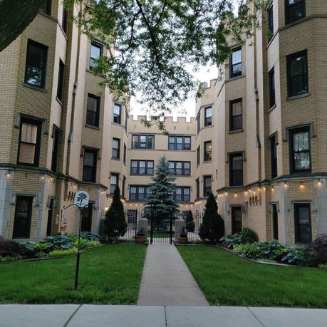 Front view of a multi-story brick apartment building with decorative lights and landscaped entrance.