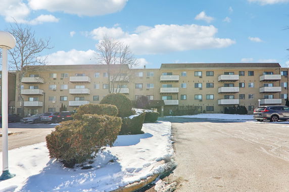 Front view of a multi-story apartment building with balconies and parking area in front.