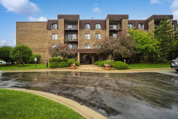 Front view of a multi-story brick building with balconies and a landscaped entrance.