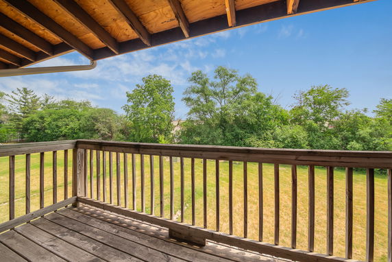 View from a wooden balcony overlooking trees and grassy area.