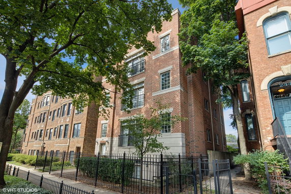Front view of a multi-story brick building with large windows and a fenced entrance.