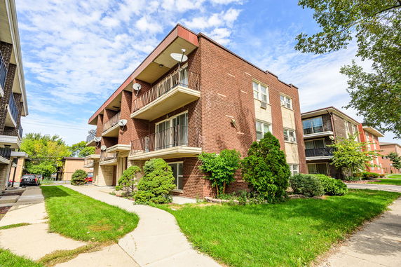 Front view of a multi-story brick apartment building with balconies and satellite dishes.