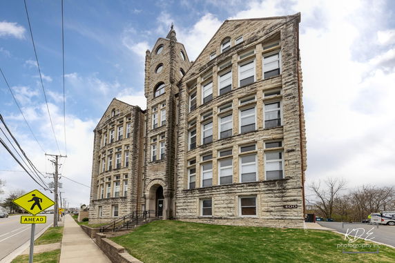Front view of a large stone building with multiple windows and a tall, central tower.