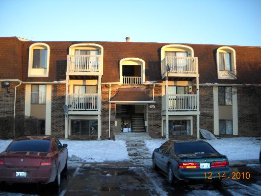 Front view of a multi-story apartment building with balconies and parked cars in front.