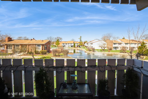 Panoramic view of a residential area with houses and a pond seen from a balcony or porch.