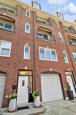 Front view of a multi-story brick building with balconies and garages on the ground floor.