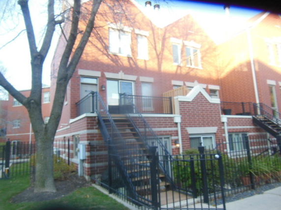 Front view of a multi-story brick townhouse with external stairs and gated entrance.