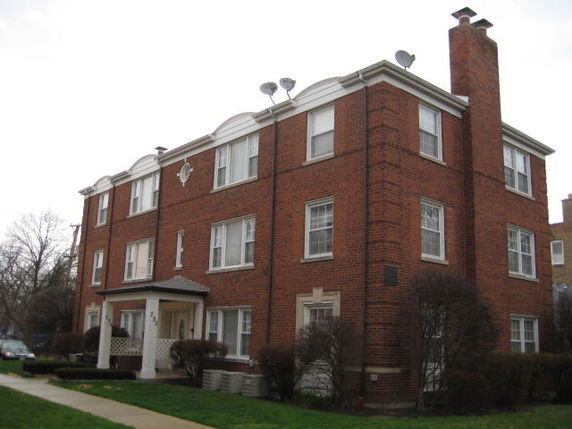 Front view of a three-story brick apartment building with multiple windows and a chimney.