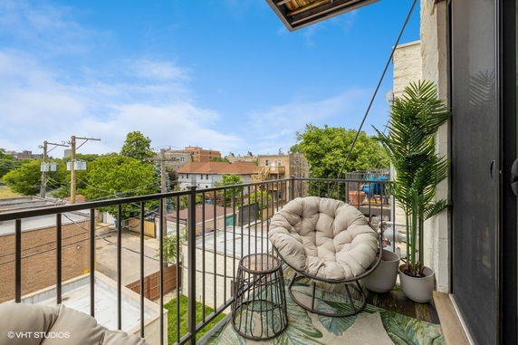 Balcony view from apartment with outdoor furniture overlooking nearby buildings and greenery.