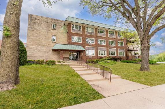 Front view of a three-story brick building with a green roof and entrance walkway.