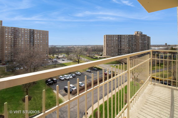 View from a building balcony overlooking nearby residential structures and parking area.