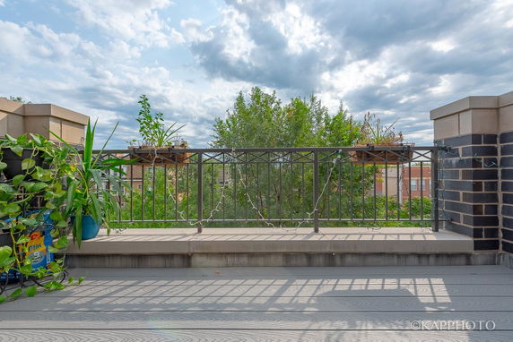 Rooftop area with railing, plants, and a view of surrounding trees and buildings.