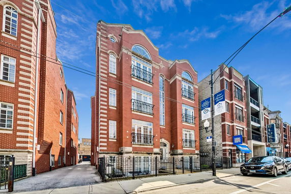 Front view of a multi-story brick building with decorative windows and wrought iron fences.
