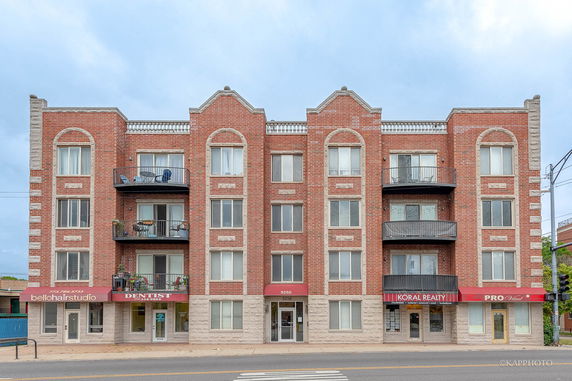 Front view of a multi-story brick building with balconies and retail units on the ground floor.