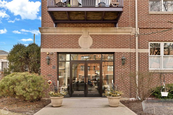 Front view of a brick building entrance with double glass doors and balcony.