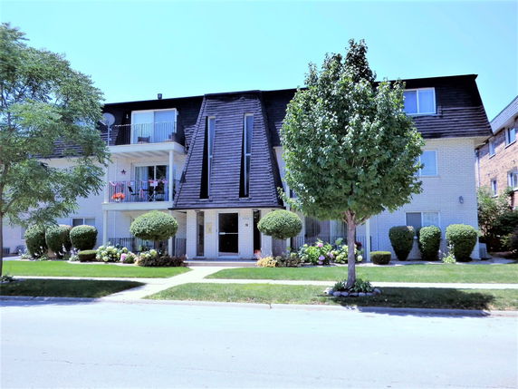 Front view of a three-story apartment building with balconies and a distinctive roof design.