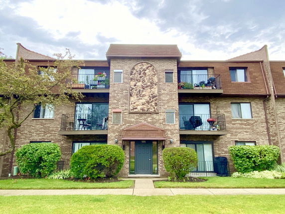 Front view of a three-story brick apartment building with balconies.