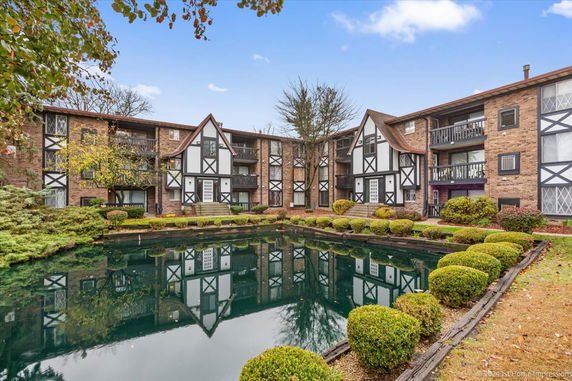 Front view of a Tudor-style residential building with balconies and a reflecting pond.
