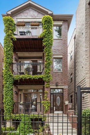 Front view of a multi-story brick building with balconies and greenery.