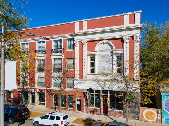 Front view of a multi-story red brick commercial building with large windows and a barber salon on the ground floor.