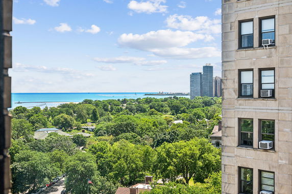 Panoramic view of a cityscape with high-rise buildings, greenery, and a distant body of water.